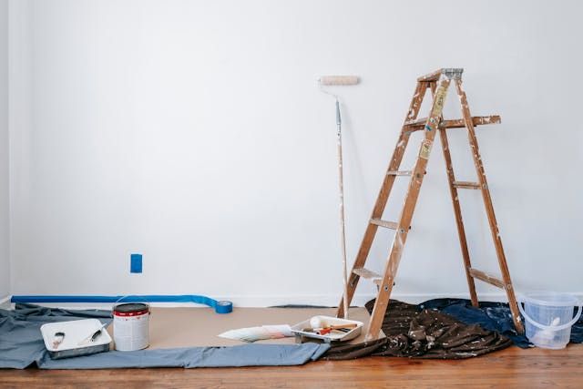 a ladder and a paint roller laid in front of a white wall